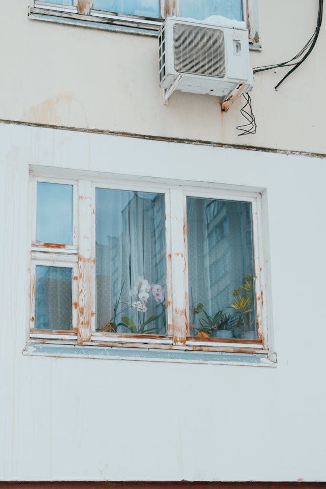 Air conditioner over a window on a white house. Image by Pexels