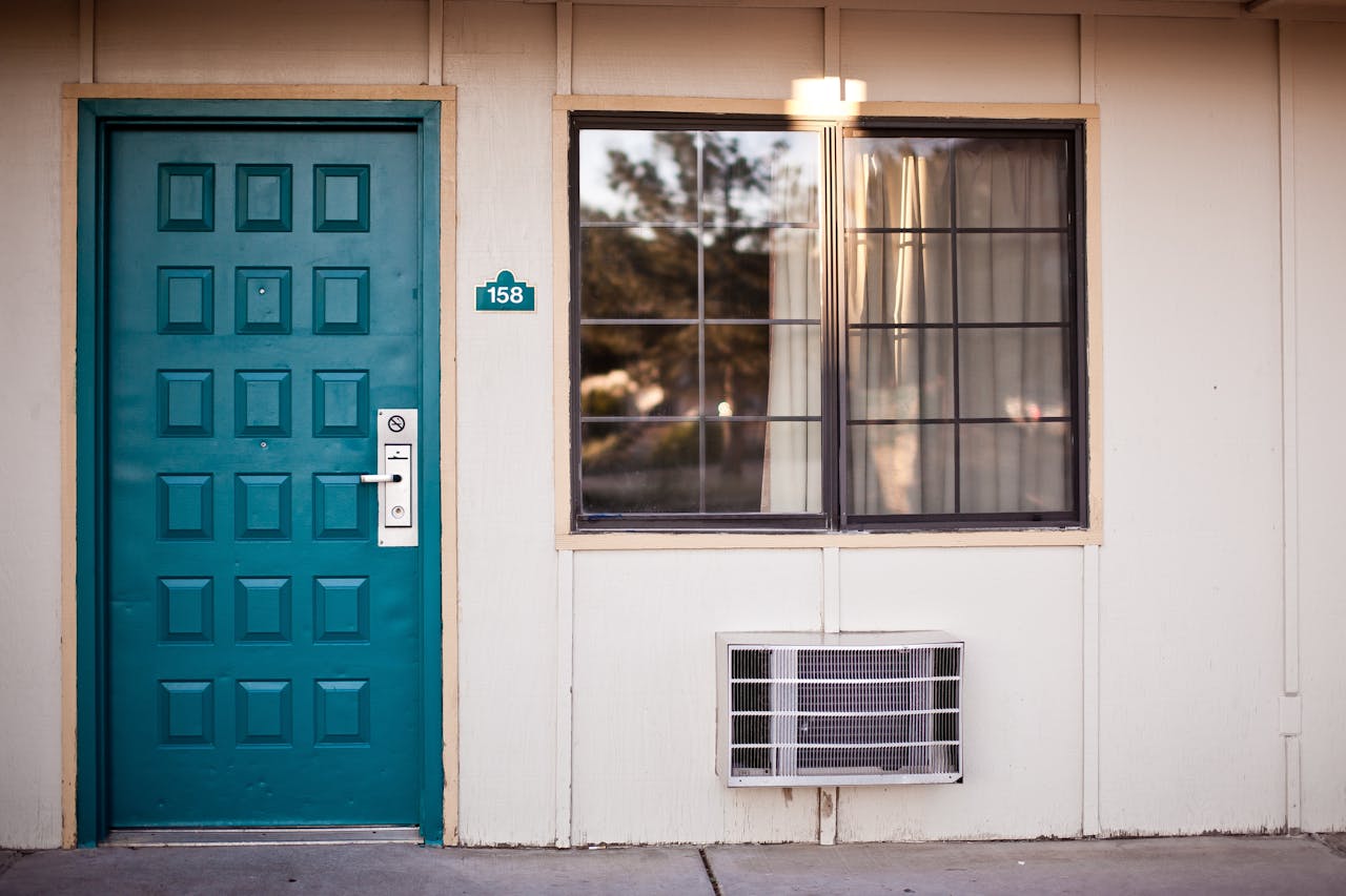 Teal door, windows, air-conditioner in wall. Image by Pexels