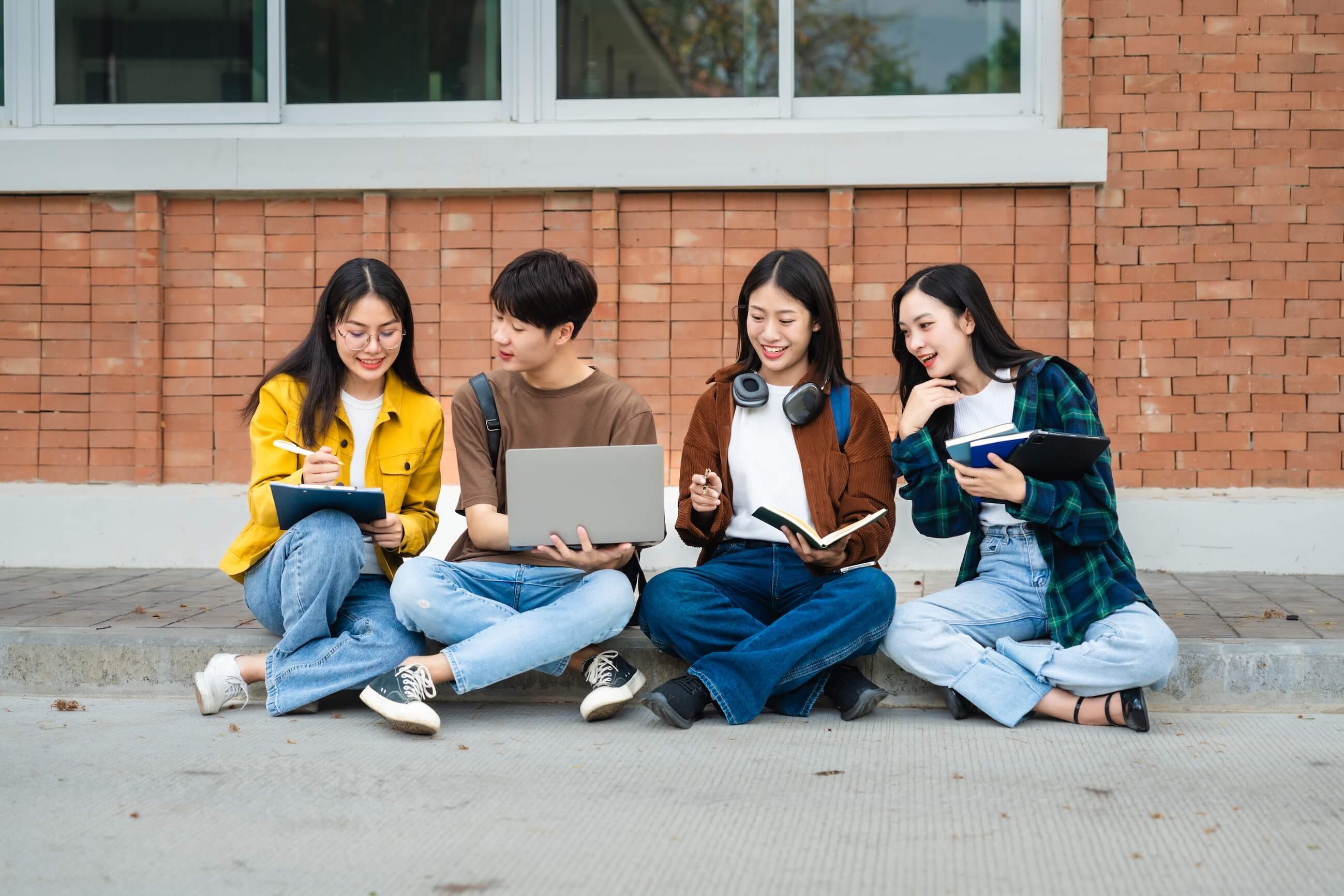 4 students sitting on the ground with laptop, books.