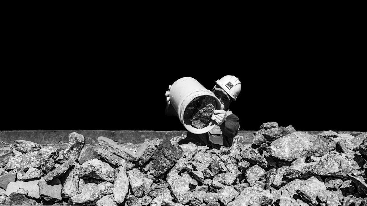 Black and white photo of a construction worker holding a 5-gallon bucket with rocks. Image by Pexels