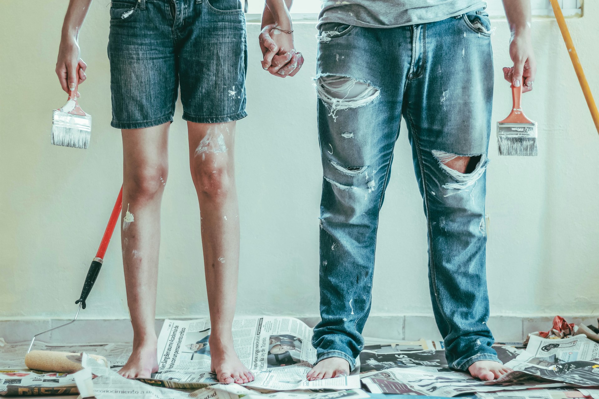 A couple holding hands, holding paint brushes. Image by Unsplash