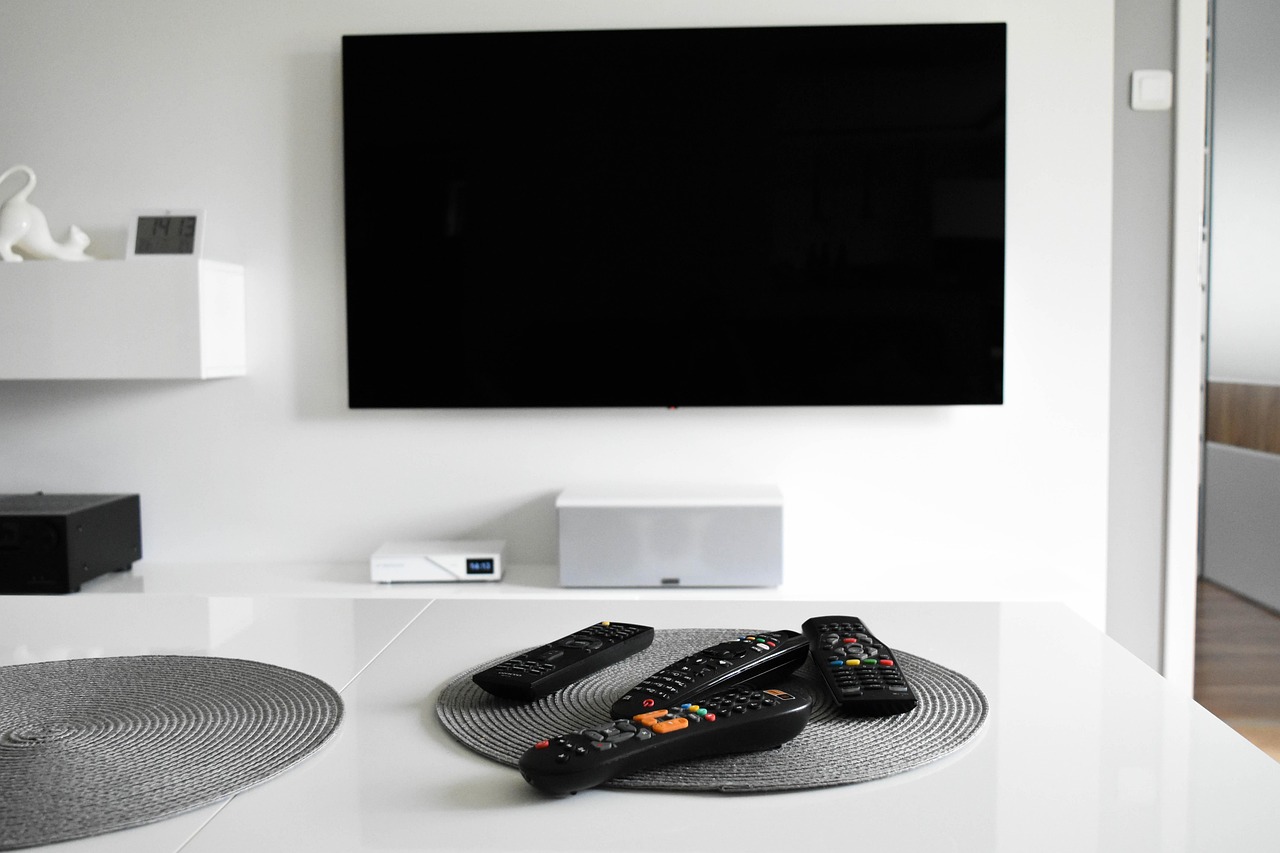 TV  on a wall, remotes on a table. Image by Pixabay.