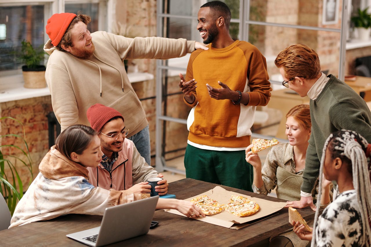 DPeople sitting and standing around a table eating pizza. Image by Pexels