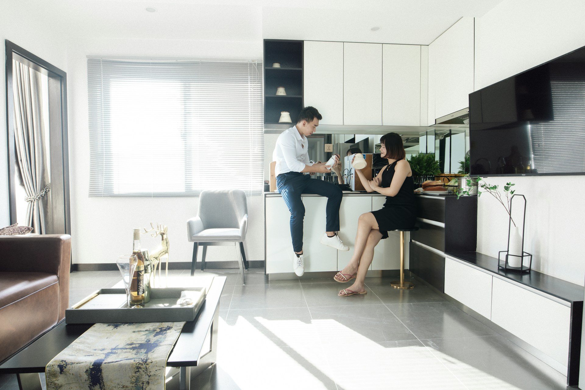 White kitchen, person in black dress sits on a stool, another oerson sitting on a counter. Image by Unsplash