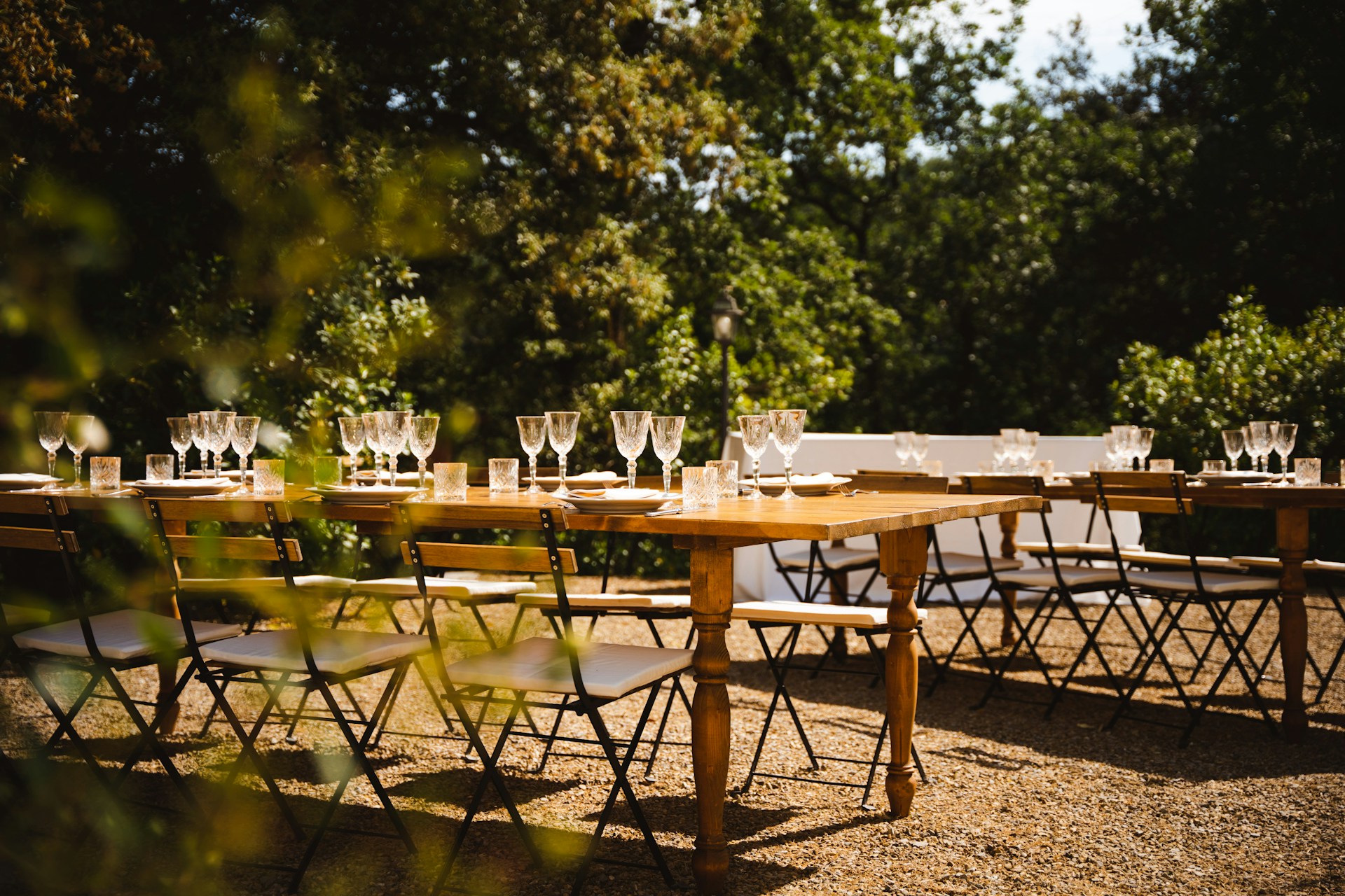 A long outdoor dining table set with empty wine glasses under string lights. Image by Unsplash