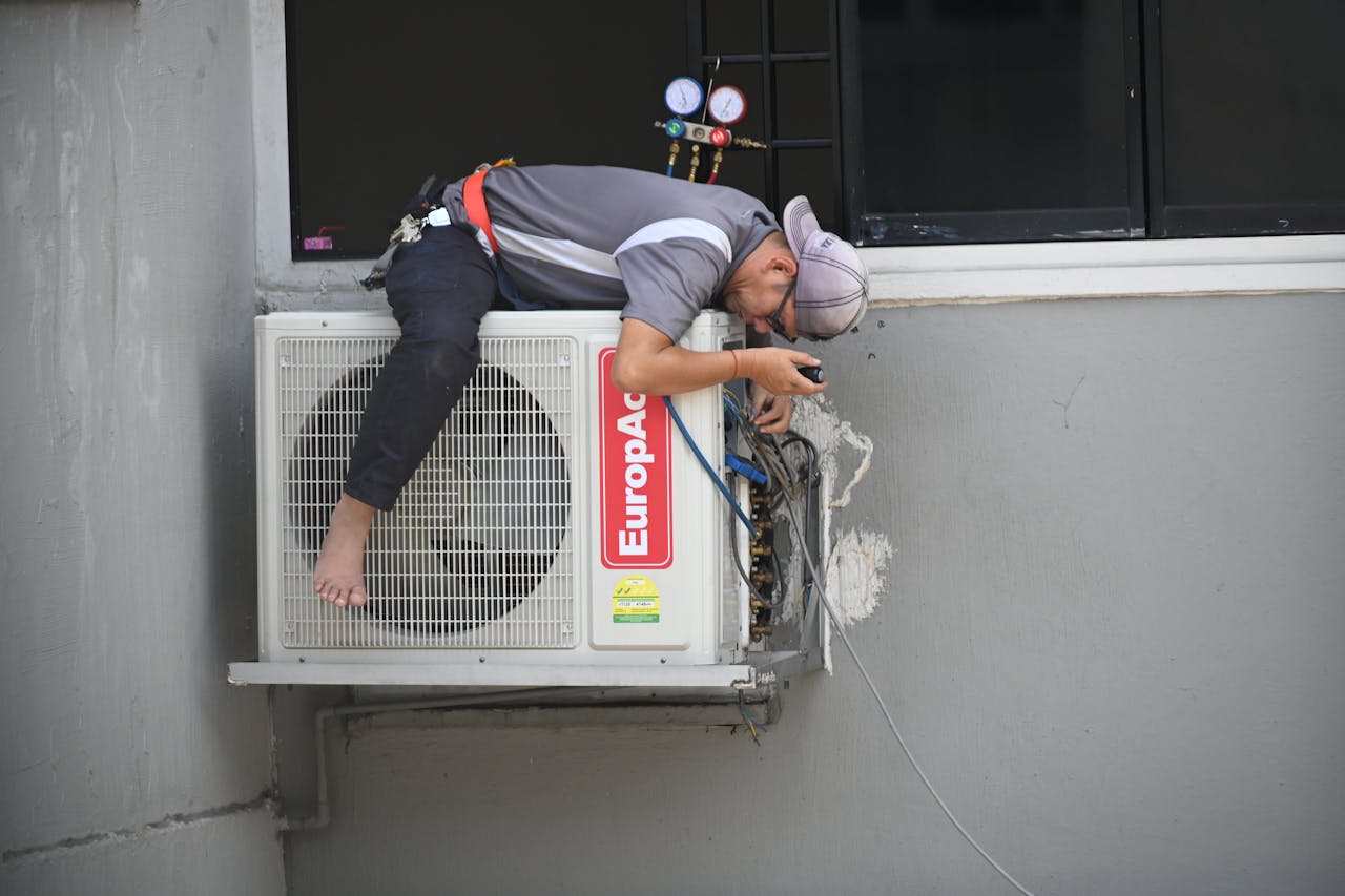 Person in a grey shirt ficing an air conditioner. Image by Pexels