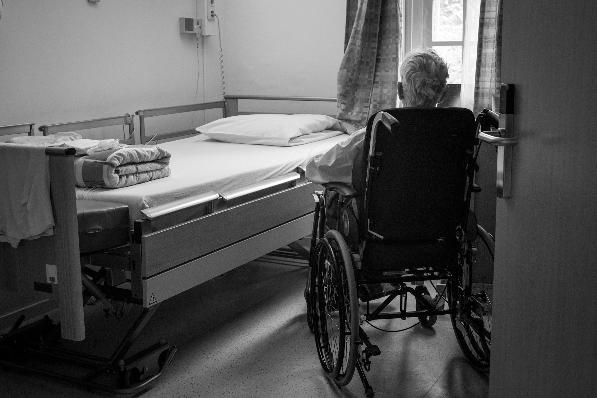Black and white photo of a hosptial bed and a person in a wheelchair. Image by Unsplash