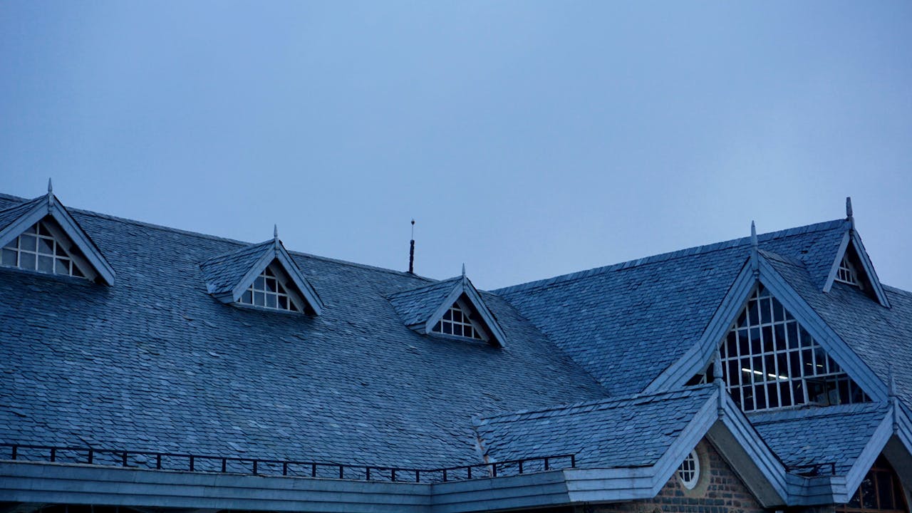 Roof of a house with multiple windows. Gray sky. Image by Pexels