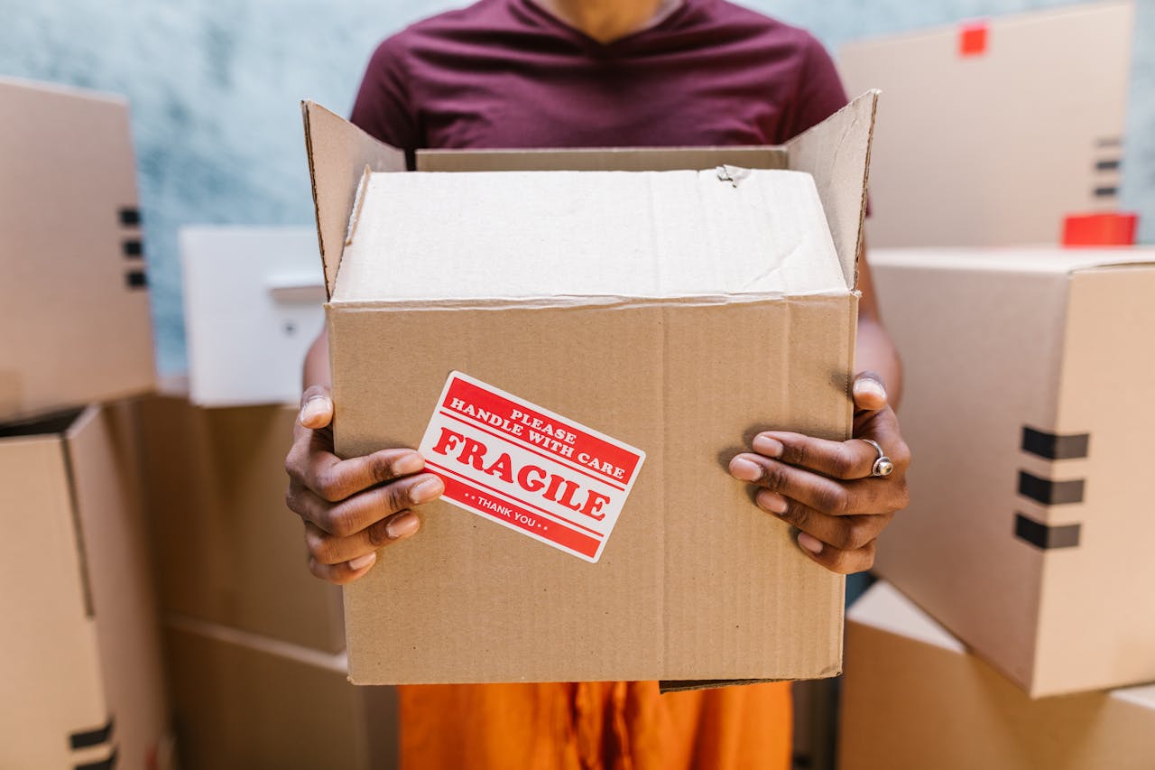 Person holding box with a red fragile label. Image by Pexels