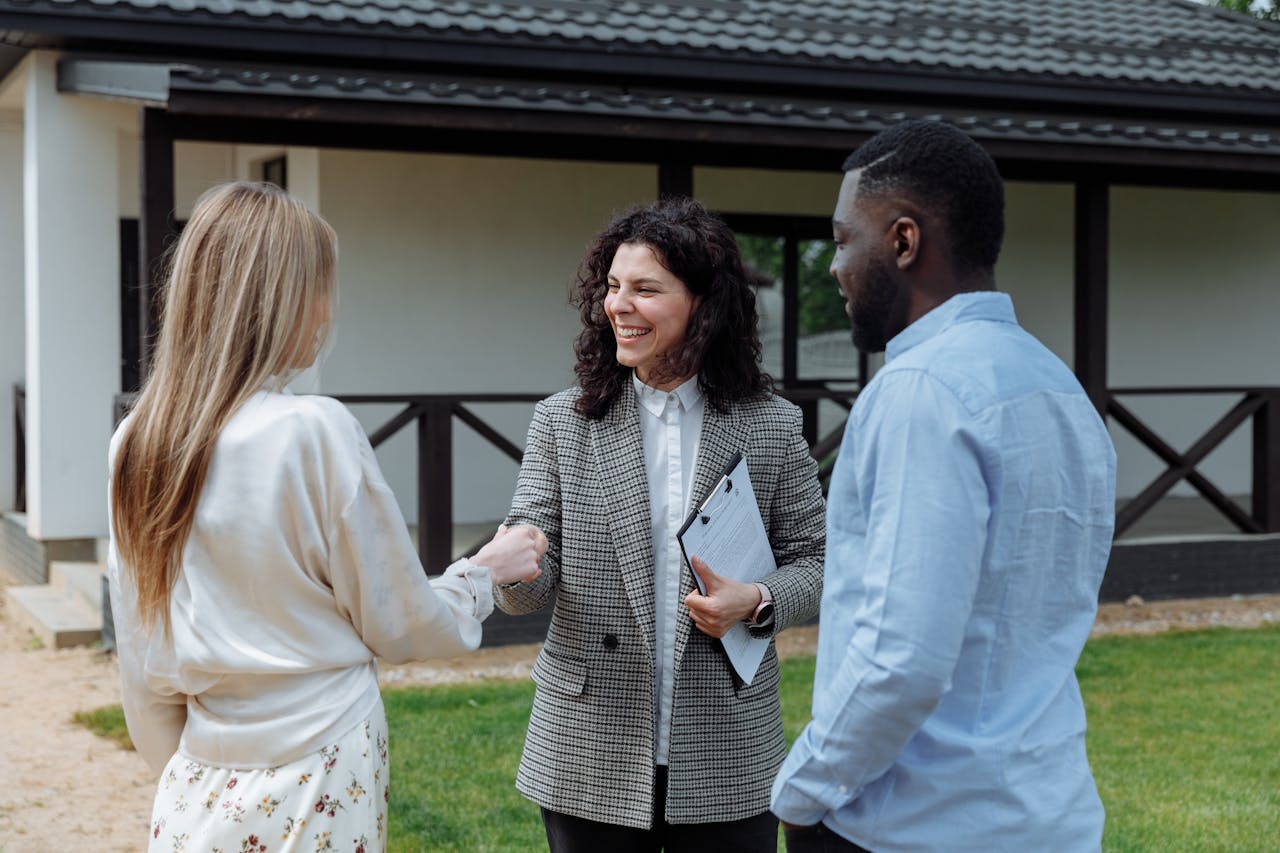A broker with a couple of people in front on a white house. Image by Pexels