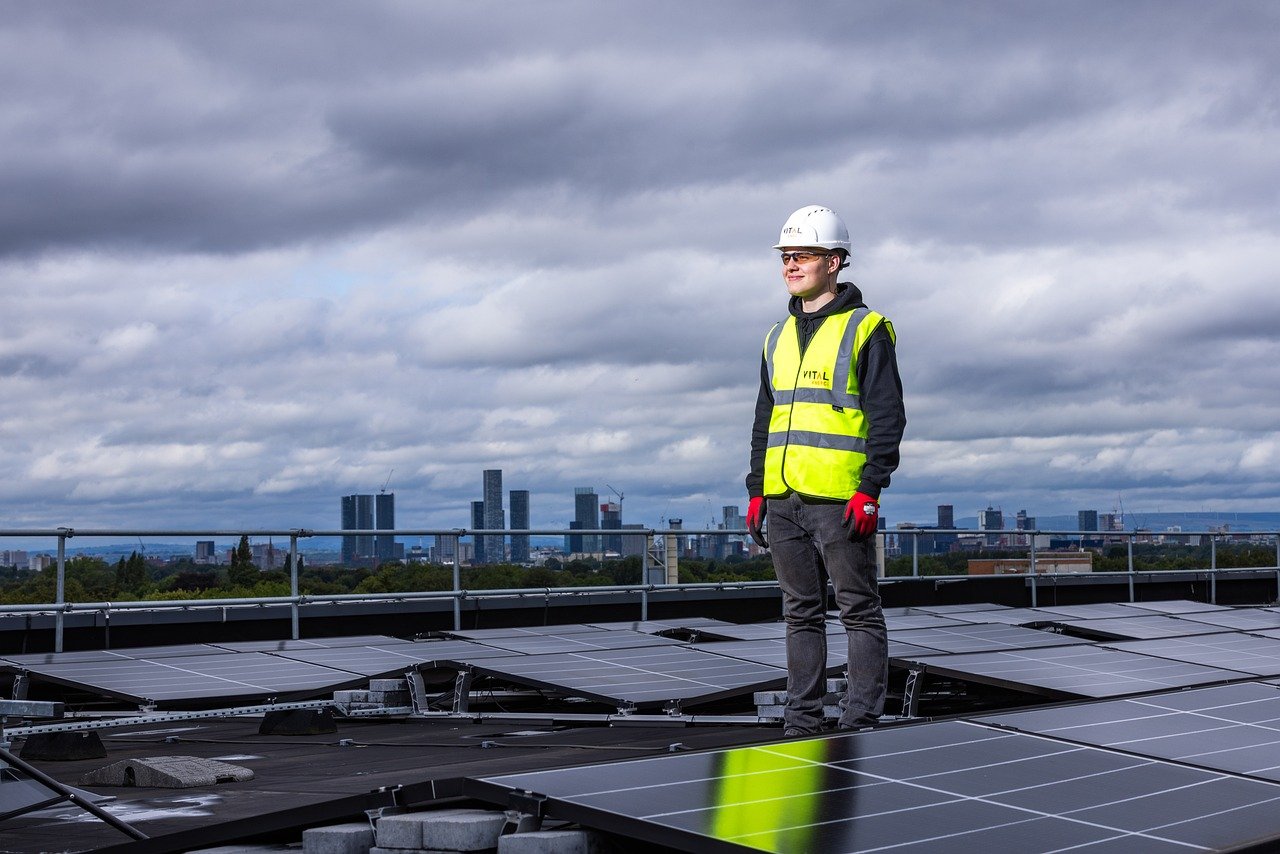 Person in yellow vest standing surrounded by solar panels. Image by Pixabay