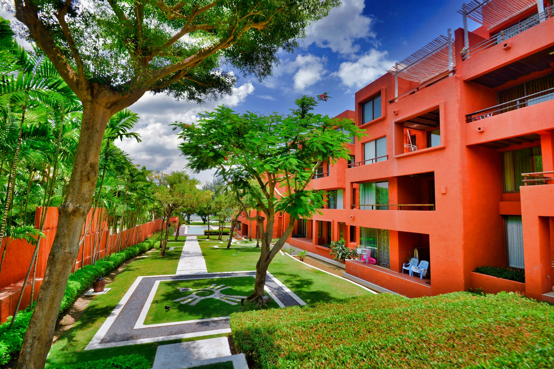 Bright red/orange apartment building with trees and grass. Image by Unsplash.