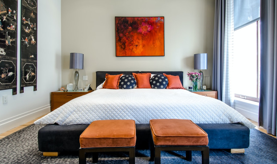 Bedroom with a bed, 2 foot stools, nighttables with lamps, wall art