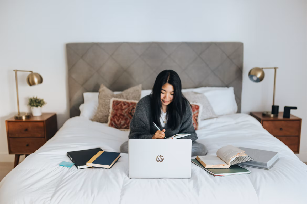girl sitting on a bed with laptop and books